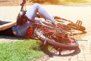A person lying on the ground with an overturned bicycle beside them on a sunny day.