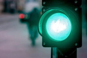 image is focusing on the green light of a stoplight with a bike rider in the distance